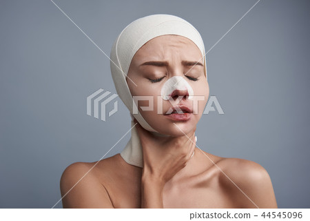 Sad woman touching her neck while recovering after plastic surgery Sad woman touching her neck while recovering after plastic surgery 44545096