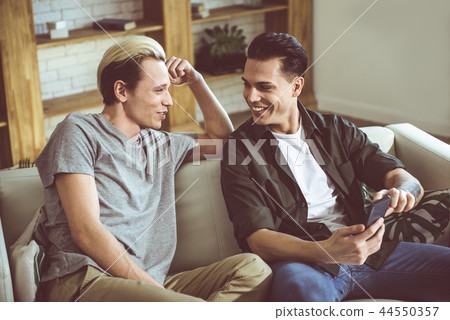 Young gay couple sitting on a couch and smiling Young gay couple sitting on a couch and smiling 44550357