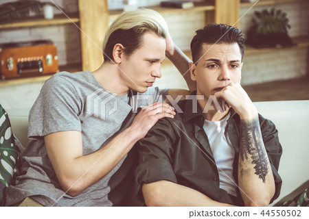 Young blond man touching shoulder of his sad boyfriend Young blond man touching shoulder of his sad boyfriend 44550502