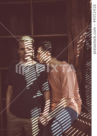 Young gay couple posing near blinds at home Young gay couple posing near blinds at home 44551418