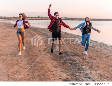 young hipster friends on beach running together 44555506