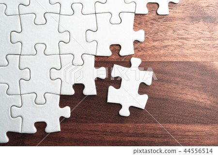Assemble a plain jigsaw puzzle on a wooden table. 44556514