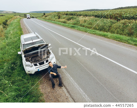 man sitting on road near broken car. trying stop car for help man sitting on road near broken car. trying stop car for help 44557265