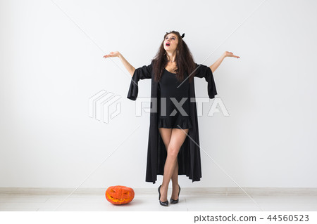 Portrait of a stylish brunette woman with halloween pumpkin over light background with copy space Portrait of a stylish brunette woman with halloween pumpkin over light background with copy space 44560523