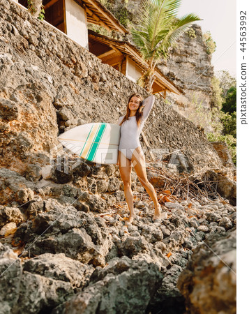 Happy surfer woman with surfboard on a rocky shore Happy surfer woman with surfboard on a rocky shore 44563992