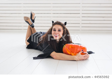 Happy gothic young woman in witch halloween costume smiling over white room background Happy gothic young woman in witch halloween costume smiling over white room background 44565092