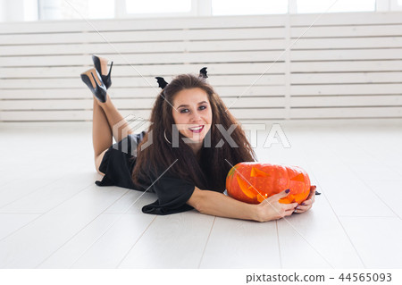 Smiling brunette woman in halloween makeup posing with carved pumpkin Smiling brunette woman in halloween makeup posing with carved pumpkin 44565093