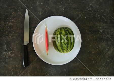 A watermelon on a white plate with a knife 44565686