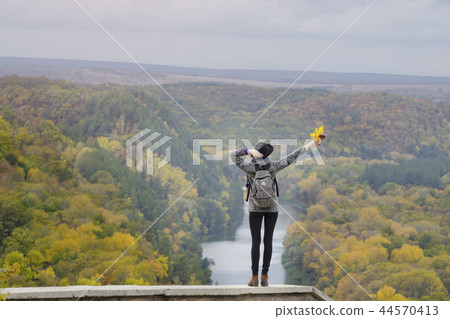 Girl with a backpack and a hat standing on a hill 44570413
