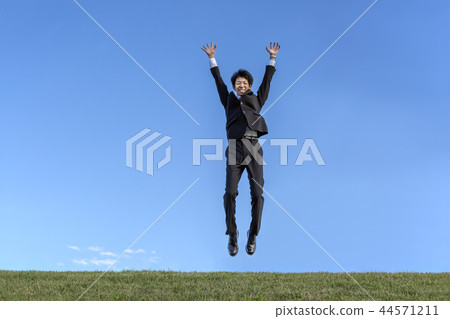 A young businessman in a suit who jumps while being surprised against the blue sky. Success, achievement, achievement, spirit image A young businessman in a suit who jumps while being surprised against the blue sky. Success, achievement, achievement, spirit image 44571211