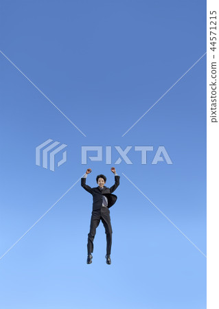 在跳躍的衣服的一個年輕商人，當驚奇反對藍天時。成功，成就，成就，精神形象 44571215