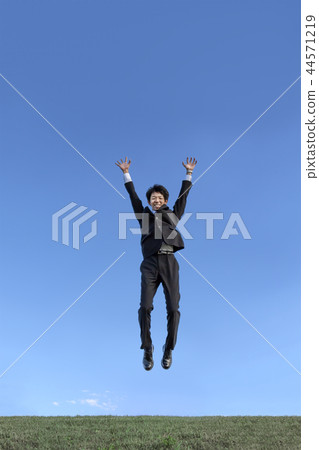 在跳躍的衣服的一個年輕商人，當驚奇反對藍天時。成功，成就，成就，精神形象 44571219