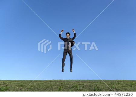 在跳躍的衣服的一個年輕商人，當驚奇反對藍天時。成功，成就，成就，精神形象 44571220