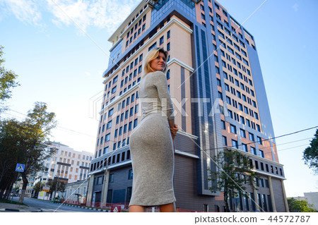 A girl with a beautiful figure in a gray dress near a tall building. 44572787