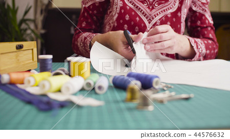 Middle-age woman hands with scissors cutting paper template. Handmade cloth. 44576632