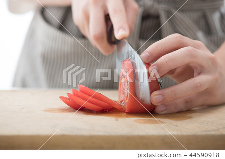 Hand of young woman cutting tomato with a kitchen knife Hand of young woman cutting tomato with a kitchen knife 44590918