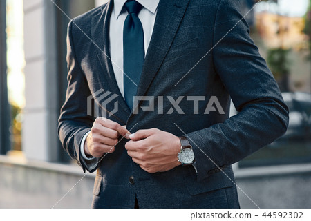 A young businessman fastens a suit jacket. He has on his hands an expensive watch. A young businessman fastens a suit jacket. He has on his hands an expensive watch. 44592302