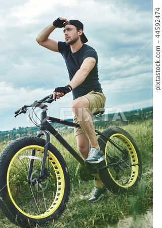 Handsome stylish guy cycling at the mountains and looks far away, bottom view 44592474