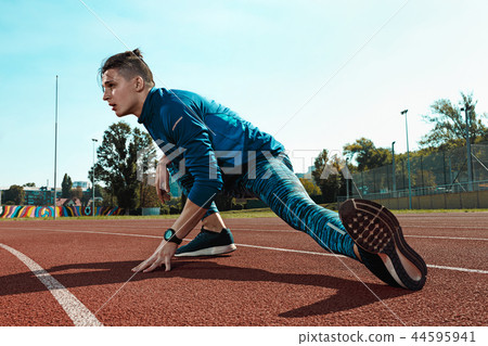 Man runner stretching legs preparing for run training on stadium tracks doing warm-up 44595941