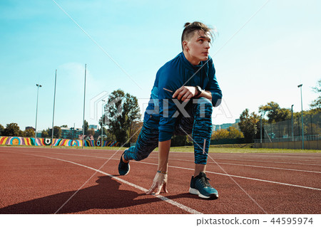 Man runner stretching legs preparing for run training on stadium tracks doing warm-up Man runner stretching legs preparing for run training on stadium tracks doing warm-up 44595974