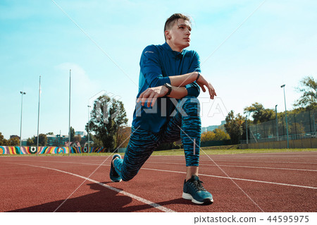 Man runner stretching legs preparing for run training on stadium tracks doing warm-up Man runner stretching legs preparing for run training on stadium tracks doing warm-up 44595975