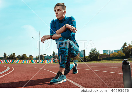Man runner stretching legs preparing for run training on stadium tracks doing warm-up Man runner stretching legs preparing for run training on stadium tracks doing warm-up 44595976