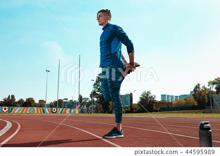 Man runner stretching legs preparing for run training on stadium tracks doing warm-up 44595989