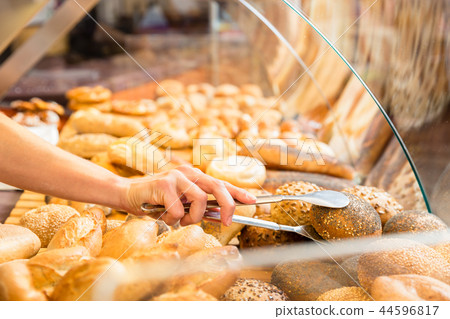 Sales woman in baker shop putting bread roll in paper bag Sales woman in baker shop putting bread roll in paper bag 44596817