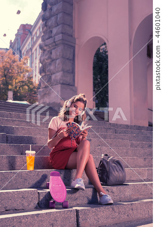 Beaming dark-haired girlfriend sitting and reading book while waiting for beloved Beaming dark-haired girlfriend sitting and reading book while waiting for beloved 44601040