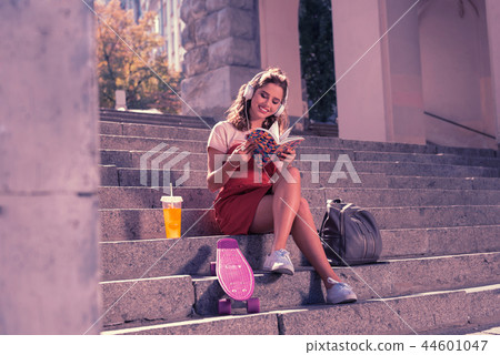 Appealing dark-haired girl reading her book and listening to music sitting outside 44601047