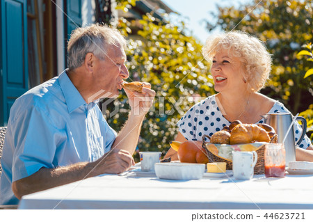 Senior woman and man having breakfast sitting in their garden outdoors Senior woman and man having breakfast sitting in their garden outdoors 44623721