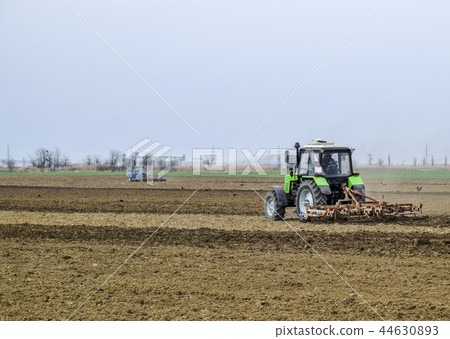 Lush and loosen the soil on the field before sowing. The tractor plows a field with a plow Lush and loosen the soil on the field before sowing. The tractor plows a field with a plow 44630893
