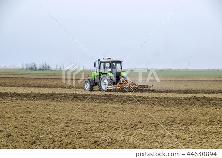 Lush and loosen the soil on the field before sowing. The tractor plows a field with a plow Lush and loosen the soil on the field before sowing. The tractor plows a field with a plow 44630894