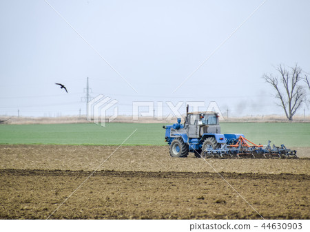 Lush and loosen the soil on the field before sowing. The tractor plows a field with a plow Lush and loosen the soil on the field before sowing. The tractor plows a field with a plow 44630903