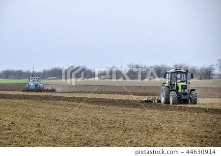 Lush and loosen the soil on the field before sowing. The tractor plows a field with a plow Lush and loosen the soil on the field before sowing. The tractor plows a field with a plow 44630914