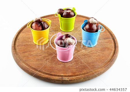 Colorful buckets with chestnuts on wooden plate Colorful buckets with chestnuts on wooden plate 44634357