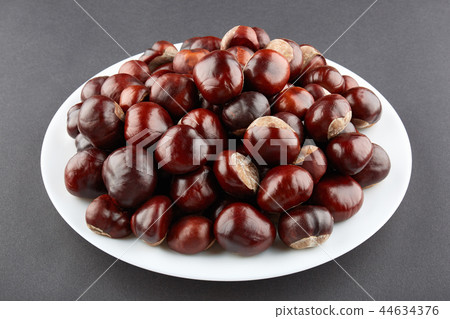 Many chestnuts on white plate. Grey background Many chestnuts on white plate. Grey background 44634376
