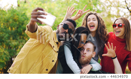 Stylish young people girls and guys are using smartphone to take selfie in park posing for camera Stylish young people girls and guys are using smartphone to take selfie in park posing for camera 44634970
