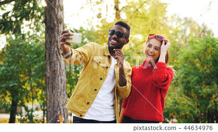 African American guy is taking selfie with female friend holding smartphone and posing with 44634976