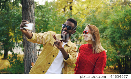 Beautiful couple African American man and Caucasian woman are taking selfie in park holding Beautiful couple African American man and Caucasian woman are taking selfie in park holding 44634977