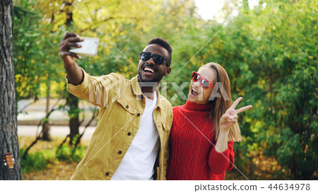Beautiful couple African American man and Caucasian woman are taking selfie in park holding Beautiful couple African American man and Caucasian woman are taking selfie in park holding 44634978