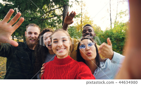 Point of view shot of joyful men and women calling friends from park making online call looking at Point of view shot of joyful men and women calling friends from park making online call looking at 44634980