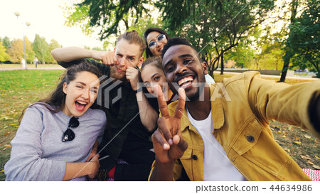 Multiracial group of friends is taking selfie in park sitting on blanket, posing and looking at Multiracial group of friends is taking selfie in park sitting on blanket, posing and looking at 44634986
