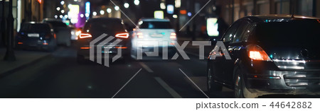 view of car in traffic jam / rear view of the landscape from window in car, road with cars, lights and the legs of the cars night view 44642882