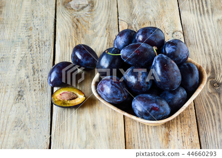 Ripe blue plums with water drops in a wooden bowl 44660293