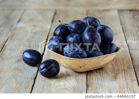 Ripe blue plums in a wooden bowl 44660297