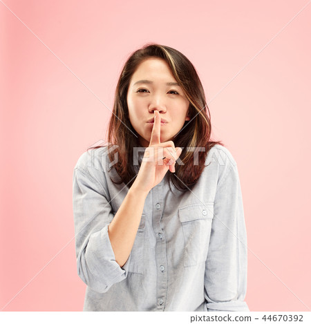 The young woman whispering a secret behind her hand over pink background The young woman whispering a secret behind her hand over pink background 44670392