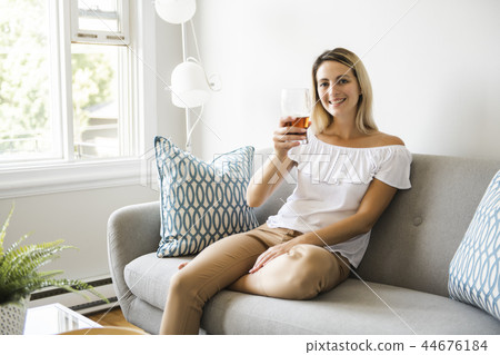 Woman drinking beer sitting on a couch in the living room at home 44676184