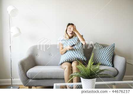Women watching TV on the sofa at home with remote control 44676237