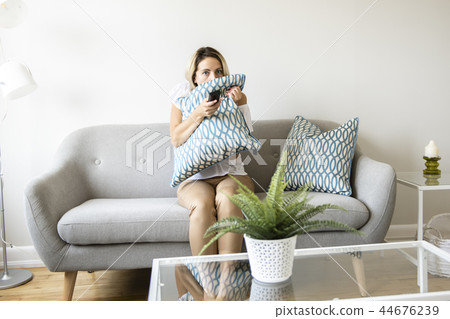 Women watching TV on the sofa at home with remote control Women watching TV on the sofa at home with remote control 44676239
